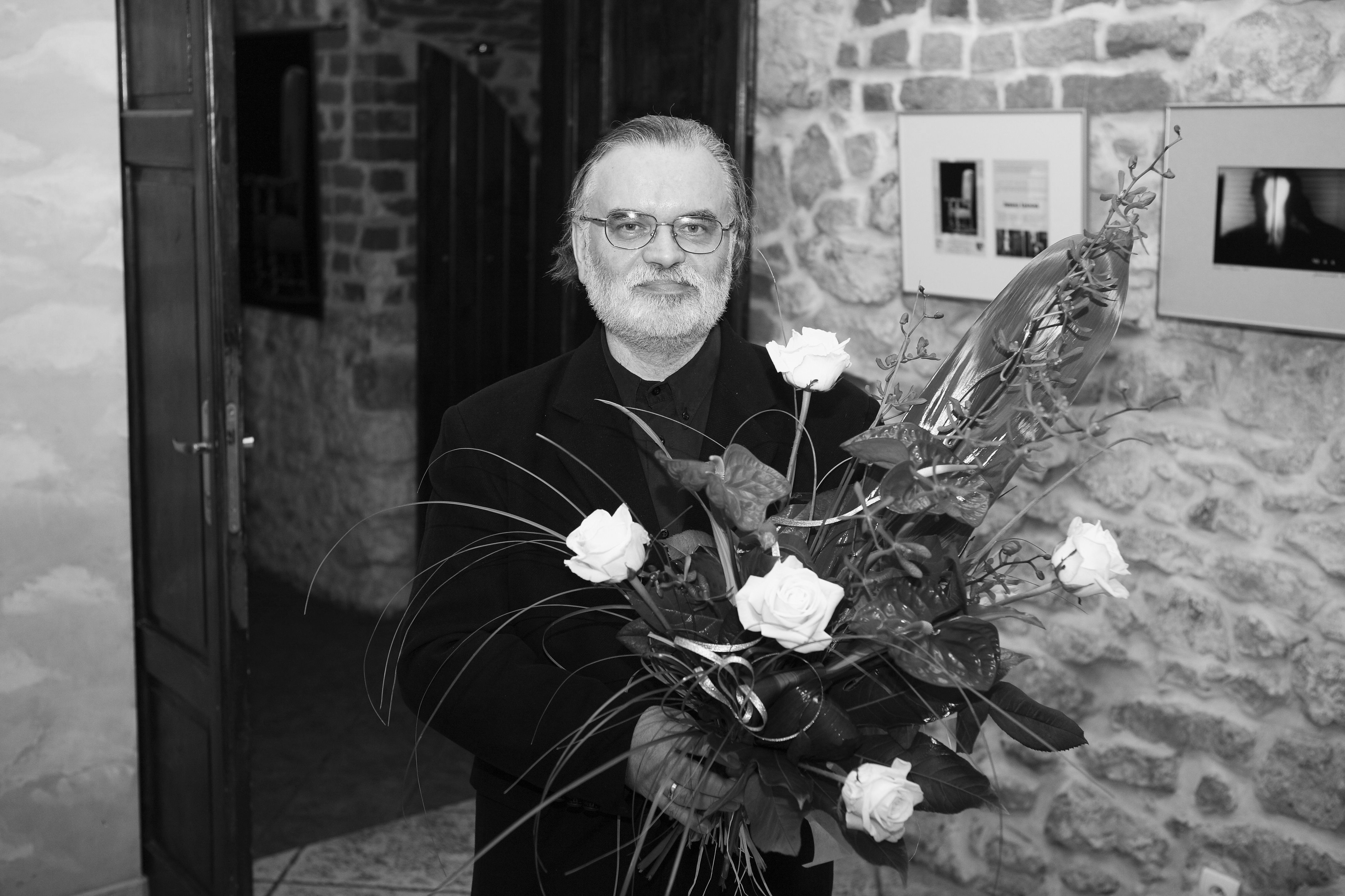 Mężczyzna z bukietem kwiatów. W tle kamieniczne wnętrze i wystawa fotografii.