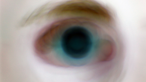 Oko z niebieską tęczówką i nienaturalnie powiększoną źrenicą, duże zbliżenie, brak ostrości