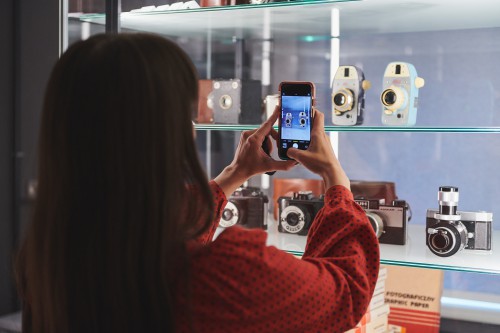 kobieta fotografuje telefonem aparaty umieszczone w gablocie