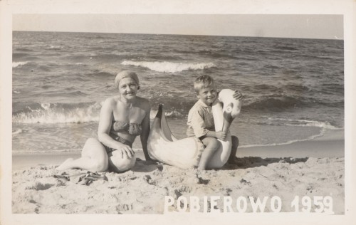 Kobieta w kostiumie kąpielowym i chłopiec na sztucznym łabędziu siedzą na plaży, napis POBIEROWO 1959