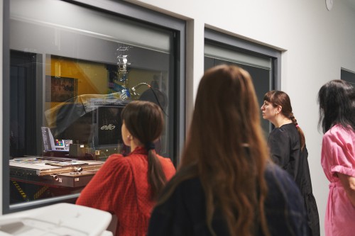 Kobiety przyglądające się przez szybę pracowni digitalizacyjnej. 