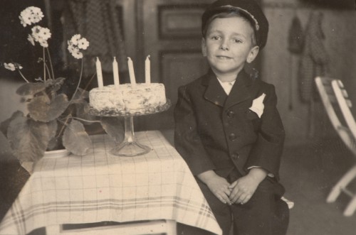 Chłopiec siedzący obok tortu z czterema świecami. 